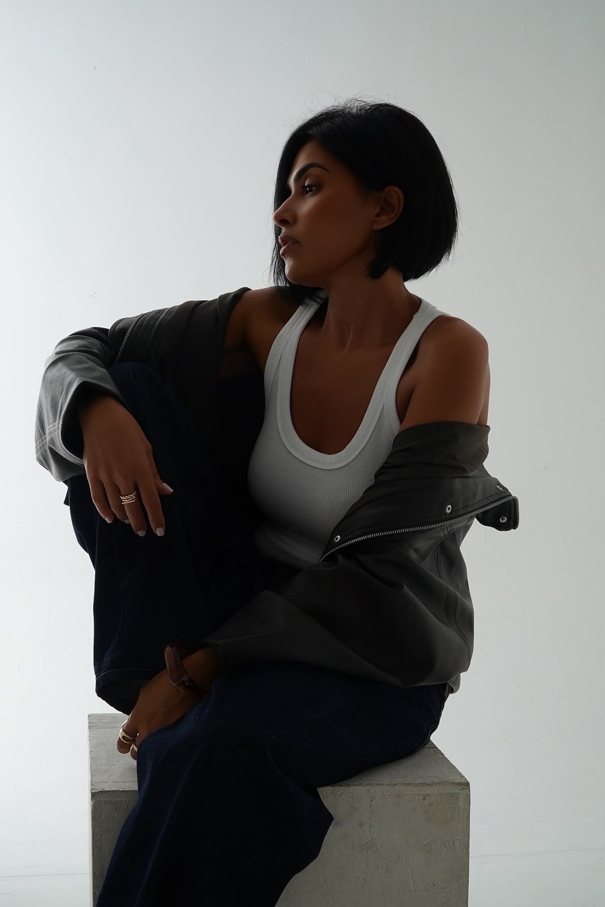 Storymum assise sur un cube en béton, veste en cuir et débardeur blanc