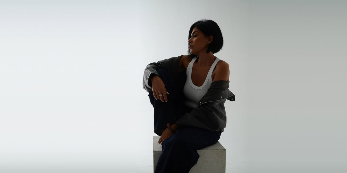Storymum assise sur un cube en béton, veste en cuir et débardeur blanc